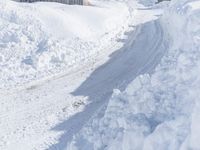 a person rides their snow board down a snowy path behind a house with large white snow covered walls
