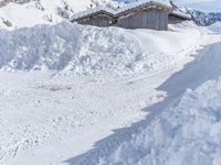 a person rides their snow board down a snowy path behind a house with large white snow covered walls
