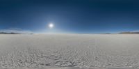 a snowboarder riding down a large snowy hill in the desert and looking up at the sun