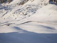a snowboarder coming down a very snowy hill side trail through some snow capped mountains