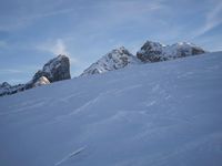 a snowboarder coming down a very snowy hill side trail through some snow capped mountains