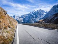 road on side of mountains with snowcapped mountains in background and sky above it