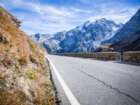 road on side of mountains with snowcapped mountains in background and sky above it