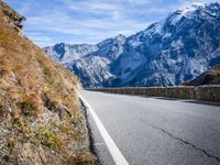 road on side of mountains with snowcapped mountains in background and sky above it