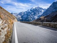 road on side of mountains with snowcapped mountains in background and sky above it