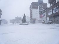 a snow storm with cars in the street and buildings on one side with snow falling