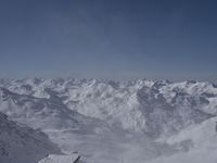 a large mountain range covered in snow and mountains with a sky background, while a person skis down a steep snowy slope with a building below it