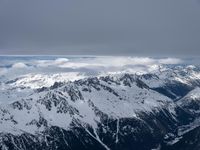 the view from an airplane of a snowy mountain range with clouds and snow capped peaks