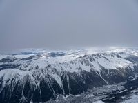 the view from an airplane of a snowy mountain range with clouds and snow capped peaks