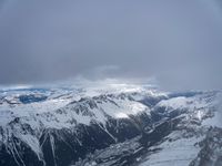 the view from an airplane of a snowy mountain range with clouds and snow capped peaks