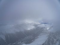 the view from an airplane of a snowy mountain range with clouds and snow capped peaks