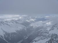 the view from an airplane of a snowy mountain range with clouds and snow capped peaks