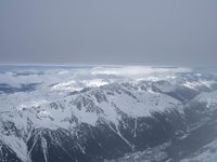 the view from an airplane of a snowy mountain range with clouds and snow capped peaks