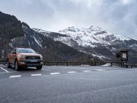 a brown car is parked at the top of a road with snowy mountains in the background