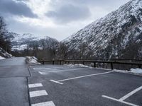 an empty car park with mountains in the background and snow on the ground and trees