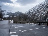 an empty car park with mountains in the background and snow on the ground and trees