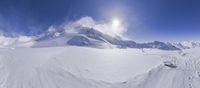 a skiier looks down on a mountain with clouds in the background and snow in the air