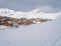 the view over a snowy mountain town and ski tracks are visible on the ski slope