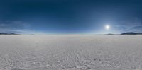 a beach with snow covering the ground, and a full sun shines bright behind the clear blue sky