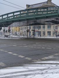 a pedestrian overpass at an intersection with snow on the ground and buildings in the background