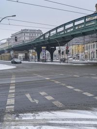 a pedestrian overpass at an intersection with snow on the ground and buildings in the background