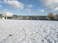 a snow covered field with the bridge in the background and a building on the other side