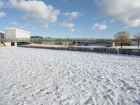 a snow covered field with the bridge in the background and a building on the other side