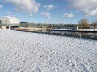 a snow covered field with the bridge in the background and a building on the other side