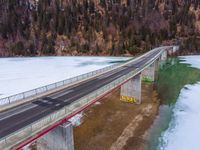 a long highway running under a bridge over a frozen lake with green waters and trees