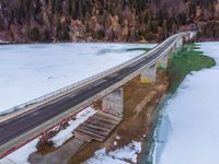 a long highway running under a bridge over a frozen lake with green waters and trees