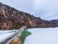 a long highway running under a bridge over a frozen lake with green waters and trees