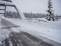 a car that is driving across a bridge in the snow by some snow covered trees