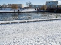 an icy waterway in the center of a snowy city yard with two people walking and walking around