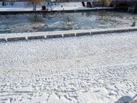 an icy waterway in the center of a snowy city yard with two people walking and walking around