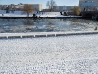 an icy waterway in the center of a snowy city yard with two people walking and walking around