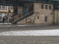 people are walking down the street in the snow by a train station with graffiti on it