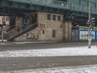 people are walking down the street in the snow by a train station with graffiti on it