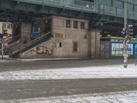 people are walking down the street in the snow by a train station with graffiti on it