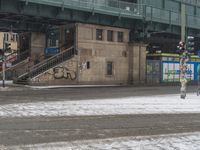 people are walking down the street in the snow by a train station with graffiti on it