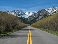 the road is paved with yellow markings and has a snowy mountain range in the background