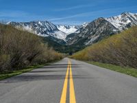 the road is paved with yellow markings and has a snowy mountain range in the background