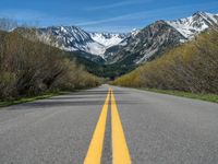 the road is paved with yellow markings and has a snowy mountain range in the background