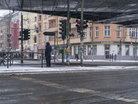 man waiting in crosswalk on snowy day near traffic lights in city center, during day