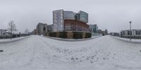 a snowy day in the city with a building in the background and benches along a side walk