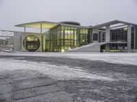 a snowy day at a large building with modern architecture and lights on in a city