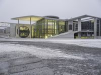 a snowy day at a large building with modern architecture and lights on in a city