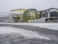 a snowy day at a large building with modern architecture and lights on in a city