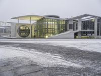 a snowy day at a large building with modern architecture and lights on in a city