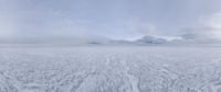 a lone person standing on the shore of an ocean covered in ice and snow with mountains in the distance
