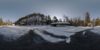 a snowy field in front of a building with several trees in the background of it